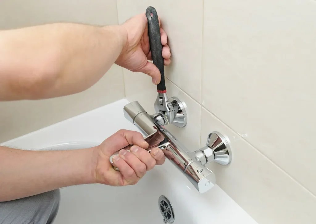 Man using a wrench to install a bathroom faucet onto a bathtub wall mount