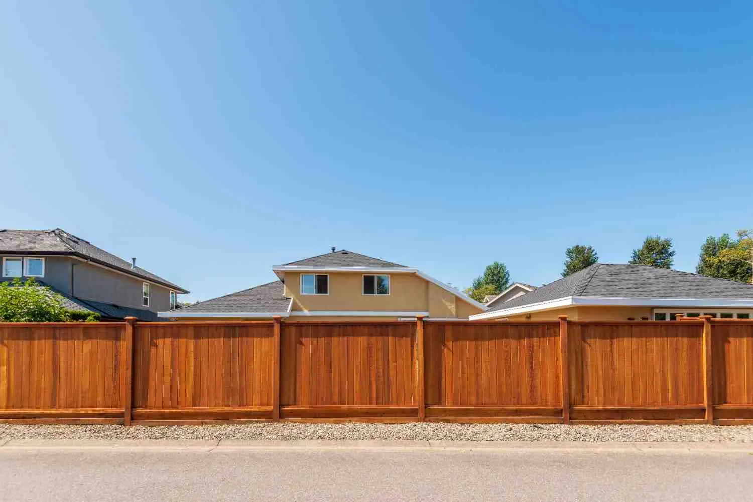 A beautiful brown cedar privacy fence in front of suburban houses, used to illustrate how much does it cost to build a fence based on material and height.