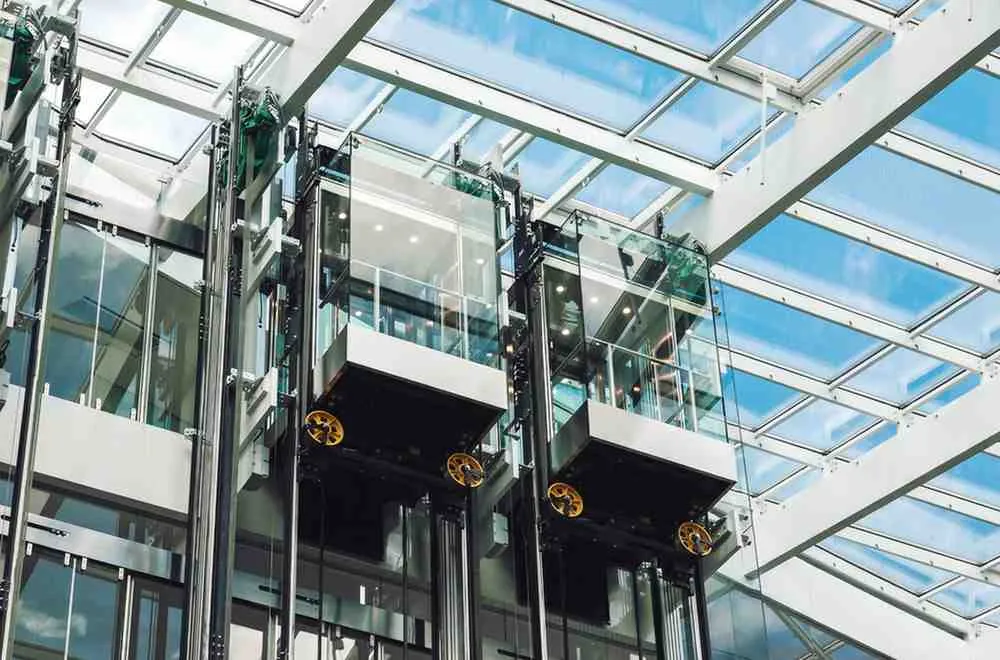 Outdoor Elevator Cost example showing modern glass outdoor elevator cabins installed in a steel frame structure with transparent walls and skylight roof.