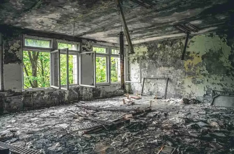Fire damaged home interior with blackened walls, broken windows, burned ceiling, and debris on the floor showing condition before rebuilding fire damaged home process.
