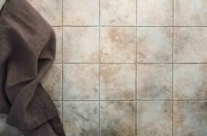 Close-up of ceramic wall tiles with stained grout lines and a cloth on the side, showing surface wear and the need to regrout tile.