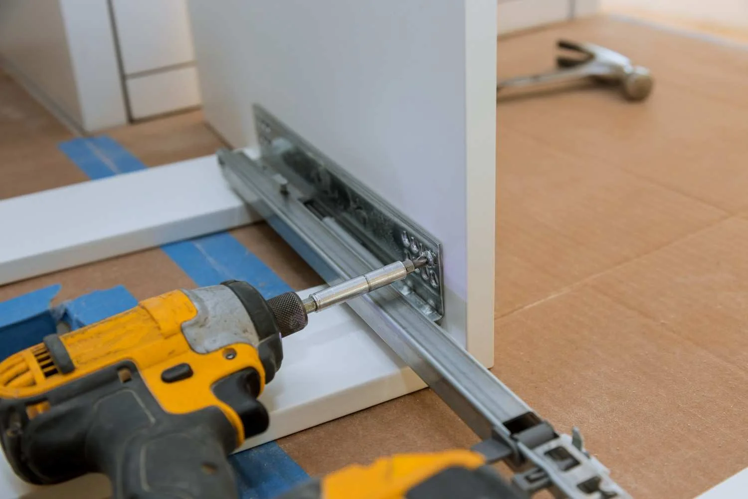 Kitchen Cabinet Toe Kick Installation with drill securing toe kick panel under kitchen base cabinets.