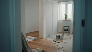 One-bedroom apartment mid-renovation with new hardwood flooring being installed, drywall, paint cans, and tools on the floor