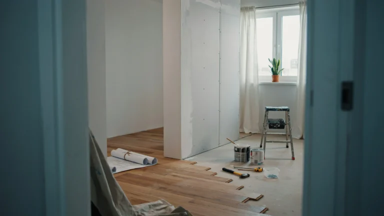 One-bedroom apartment mid-renovation with new hardwood flooring being installed, drywall, paint cans, and tools on the floor