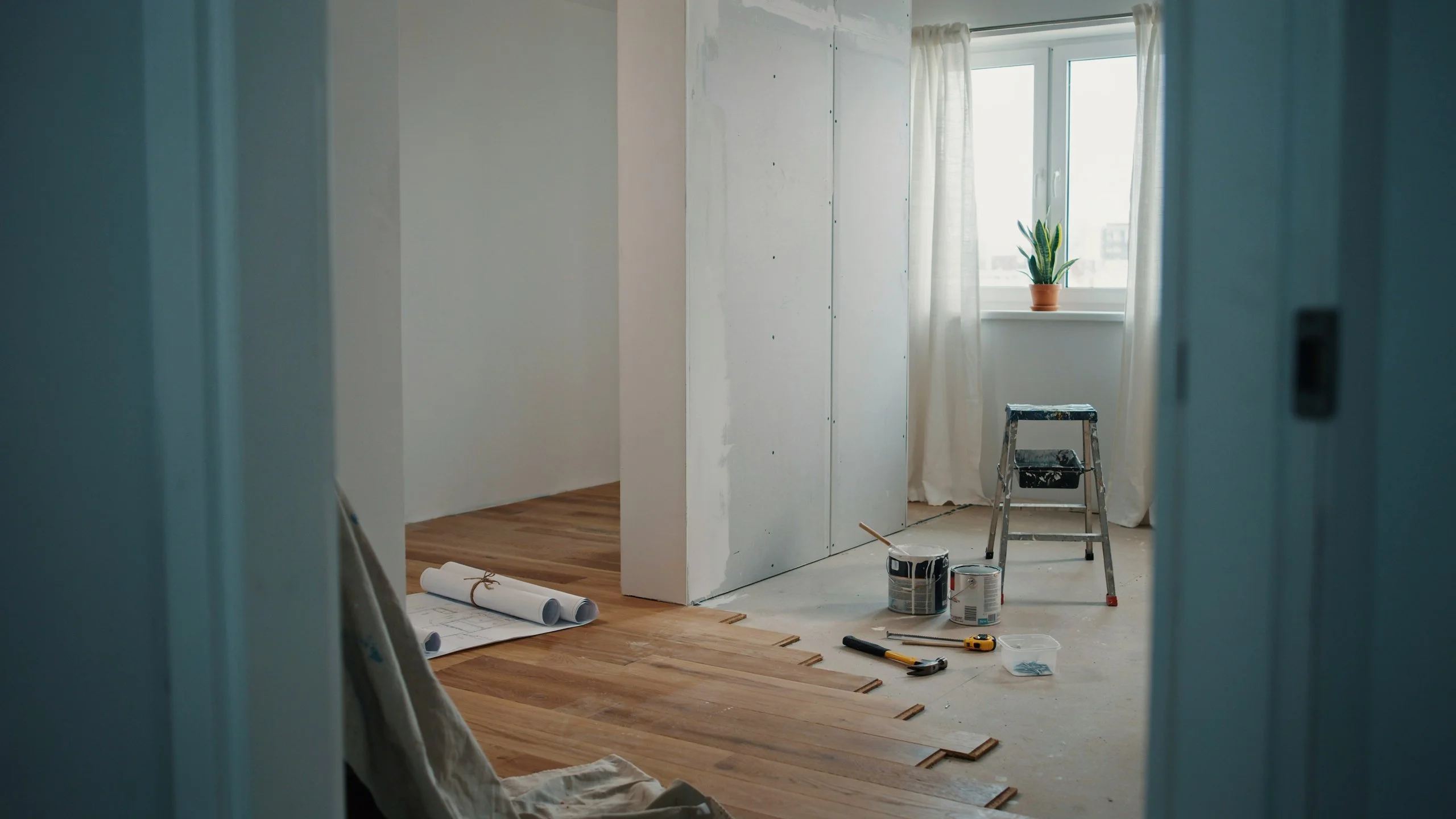 One-bedroom apartment mid-renovation with new hardwood flooring being installed, drywall, paint cans, and tools on the floor
