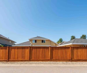 A beautiful brown cedar privacy fence in front of suburban houses, used to illustrate how much does it cost to build a fence based on material and height.
