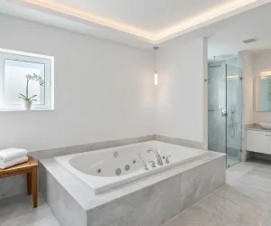 Modern luxury bathroom showing how much does a jacuzzi bath remodel cost — white jetted tub with marble surround, pendant lighting, glass shower, and double vanity