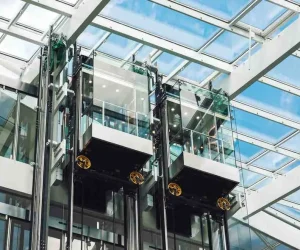 Outdoor Elevator Cost example showing modern glass outdoor elevator cabins installed in a steel frame structure with transparent walls and skylight roof.