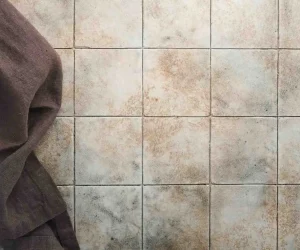 Close-up of ceramic wall tiles with stained grout lines and a cloth on the side, showing surface wear and the need to regrout tile.